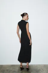 Vestido largo sin mangas con cuello subido, confeccionado con una parte superior lisa y falda de tul con caída fluida. Cuenta con cierre de cremallera oculta en la espalda.