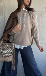 Sweater de punto color beige con bordado de flores blancas en el frente y las mangas, cuello redondo y puños acanalados.