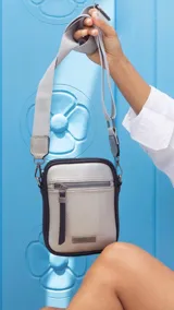 Phone bag color marrón claro con laterales beige, bolsillo frontal con cierre y tirador con flecos. Tiene espacio para celular y billetera, y correa de galón regulable y desmontable.