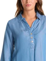 Blusa de lyocell color azul claro, con cuello camisero, escote en V y cierre frontal parcial con botones. Presenta mangas tres cuartos amplias y un corte holgado con aberturas laterales en el ruedo.
