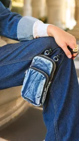 Phone bag de tela con efecto denim desgastado, con compartimento principal y bolsillo frontal con cierre. Incluye correa elástica regulable y desmontable, con detalles en negro.