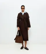 Trench coat largo color marrón chocolate, confeccionado en tejido tipo paño, con solapas amplias, cierre frontal cruzado con cinturón de la misma tela para anudar y detalles de trabillas en los hombros y puños.