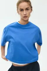 Remera de corte boxy y holgado, color azul, confeccionada en suave punto de algodón. Presenta cuello redondo, hombros caídos y mangas cortas que llegan hasta el codo.