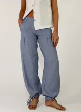 Pantalón de lino color beige, de corte holgado tipo jogger con puños ajustables con cintas en los tobillos, bolsillos laterales y cierre frontal con botón y cremallera.