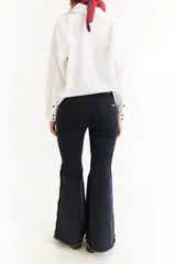 Jean de corte oxford con tiro medio, confeccionado en denim negro. Presenta recortes curvos en las piernas y detalle de botones metálicos en los laterales de la botamanga.