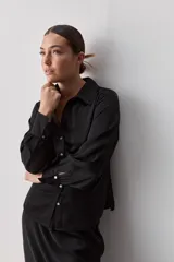 Camisa blanca de manga larga con textura suave y caída liviana, cuello camisero, puños anchos y fruncidos sutiles en los hombros.