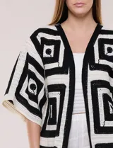 Cardigan largo confeccionado en tejido de punto calado estilo crochet, de color amarillo y blanco, con diseño geométrico de cuadrados, mangas amplias tipo kimono y corte abierto al frente.