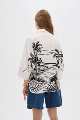 Camisa de viscosa de corte holgado, color blanco con estampado negro de paisaje con palmeras, cuello camisero y cierre frontal con botones.