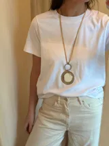 Collar largo con cordón de cuero color beige y dije circular plateado con centro espejado.