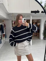 Buzo de tejido de punto grueso en color gris con rayas horizontales en color crema, de corte holgado, cuello redondo y mangas largas.