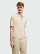 Remera polo de punto fino color beige, con cierre frontal parcial y cuello clásico. Presenta mangas cortas con terminación en rib y diseño de calce ajustado.