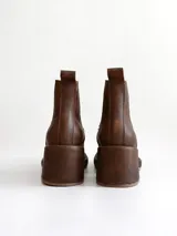 Bota tipo chelsea de cuero color chocolate con acabado texturizado, plataforma y taco cuadrado. Presenta paneles elásticos laterales en color negro.