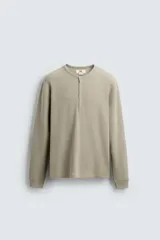 Camiseta de manga larga con cuello redondo y tapeta de botones a presión, confeccionada en tejido waffle.