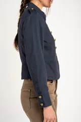 Chaqueta corta color beige de algodón, de inspiración militar con cuello mao y doble botonadura frontal con botones metálicos dorados.