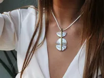 Collar con dije geométrico de nácar y bronce, con cordón blanco.