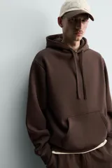 Sudadera con capucha de corte relajado, confeccionada en tejido de algodón con interior perchado. Presenta mangas largas, bolsillo frontal tipo canguro y terminaciones en rib.