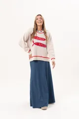 Sweater tejido color crudo con cuello redondo y mangas largas. Presenta dos peces rojos con detalles en azul bordados en el frente. Tiene ribete ondulado rojo en cuello, puños y ruedo.