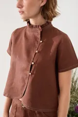 Blusa de lino verde de manga corta y corte recto, con cuello alto con volado y cierre frontal cruzado con botoncitos dorados.
