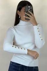 Polera de hilo blanca de cuello alto y manga larga, con detalle de botones dorados en los puños. Tejido de punto acanalado ajustado al cuerpo.