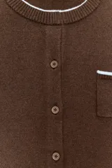 Chaqueta de punto color marrón con cuello redondo, manga larga y cierre frontal con botones. Presenta un bolsillo delantero tipo plastrón y detalles de ribetes en color celeste en el cuello y el bolsillo.