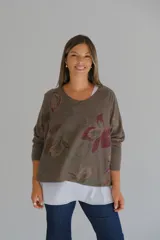 Sweater de corte amplio con diseño de doble capa, que presenta una capa superior en tono chocolate con estampado floral y una capa inferior en color blanco. Posee escote en V y mangas largas con terminaciones desflecadas.
