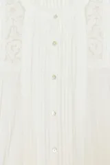 Camisa blanca de algodón con cuello redondo y manga por debajo del codo abullonada. Presenta detalles de bordados a tono y cierre frontal con botones.