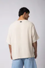 Remera de corte oversize confeccionada en tejido texturado tipo lino, de color beige, con cuello redondo amplio y mangas cortas de calce relajado.