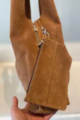Bolso tipo hobo grande confeccionado en cuero vacuno color marrón, con costura central vertical y placa metálica con el logo de la marca Pecarí.