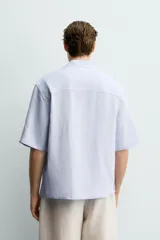 Camisa tipo kimono de corte relaxed fit, color celeste, confeccionada en tejido fluido de viscosa y lino. Presenta cuello con solapas de muesca, manga corta y cierre frontal cruzado con doble botonadura.