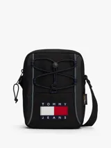 Cartera reporter de estilo urbano color negro, con compartimento principal con cierre, cordones elásticos ajustables en el frente y correa ajustable. Presenta el logo de la marca en un parche frontal y etiqueta lateral de Cordura.