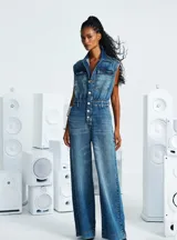 Enterito de jean azul con corte amplio, cuello camisero, sin mangas, con bolsillos delanteros y cierre frontal con botones.