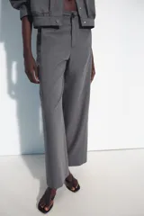 Pantalón de tiro medio color gris, con corte recto, bolsillos delanteros y detalle de costura vertical en el frente. Cuenta con cierre frontal de cremallera y botón.