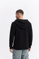 Canguro de punto negro con capucha, de corte relajado y textura acanalada. Presenta puños y ruedo tejidos.