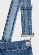 Jardinera de denim en color azul medio, con diseño de corte recto, tirantes ajustables con hebillas metálicas, cierre de botones laterales y bolsillos funcionales.