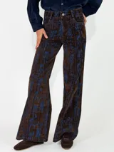 Pantalon de corte recto y tiro alto, confeccionado en tela con textura tipo pana o denim con un estampado abstracto en tonos marrones y azules.