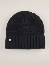 Gorro tipo beanie color azul marino, con textura de punto en relieve y borde acanalado. Incluye un pequeño aplique metálico circular con el logo de la marca en el frente.