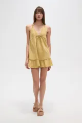 Vestido mini blanco de algodón, con escote en V, tirantes finos que se anudan en el cuello, ajuste con cordón en la cintura y volados en el ruedo.