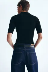 Top de punto pointelle acanalado en color negro, con cuello camisero, manga corta y tapeta con botones frontales.