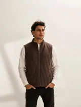 Chaleco de hombre color marrón con diseño capitoneado en rombos, cuello alto y cierre frontal con cremallera.