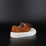 Zapatillas acordonadas tipo championes, confeccionadas en cuero color suela y blanco, con base de goma blanca.