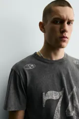 Camiseta de corte slim fit, cuello redondo y manga corta, color gris oscuro con efecto lavado. Presenta un gran estampado frontal con el número "74" en blanco desgastado y pequeños estampados circulares en los hombros.