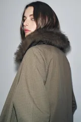 Trench reversible de corte recto con cuello de solapa y aplicación de pelo sintético extraíble. Presenta cierre frontal con botones, manga larga y bolsillos laterales ocultos en las costuras.