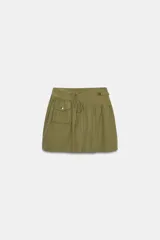 Falda corta de tiro medio en color verde militar. Presenta un diseño con volumen, pliegues, un bolsillo de plastrón en el delantero y detalle de trabilla con hebilla metálica en la cintura. Incluye cierre lateral con cremallera oculta.
