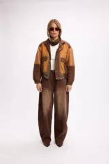 Chaqueta bomber de diseño combinado en tonos tierra, confeccionada con paneles de gamuza y detalles en cuero sintético. Presenta cierre frontal con broches metálicos, bolsillos frontales con tapa y puños elásticos.