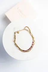 Pulsera dorada de acero quirúrgico con doble cadena, una de eslabones grandes y otra con cuentas rojas.