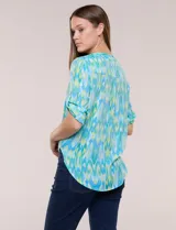 Blusa camisera de estilo casual confeccionada en mezcla de rayón y poliéster, con estampado multicolor en tonos turquesa, verde y celeste. Presenta escote en V con cuello mao, abotonadura frontal con botones nacarados, bolsillos aplicados en el pecho y mangas tres cuartos con presilla para arremangar. Cuenta con ruedo curvo y picos frontales diseñados para anudar en la cintura.