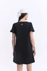 Vestido corto negro con escote en V, mangas cortas abullonadas, silueta suelta y costuras visibles en el frente y la espalda.