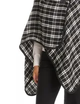 Ruana tejida con diseño de cuadros en blanco y negro, con borde ribeteado y cierre frontal tipo trenca con detalle de cuero sintético.