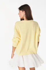 Sweater de punto color amarillo claro, con cuello redondo y diseño holgado. Cuenta con un bordado central en el pecho que representa un sol con su reflejo y la inscripción "PETRA" en tonos naranjas.