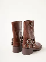 Botas de caña media Mutma modelo Mota, confeccionadas en cuero texturado color marrón. Presentan diseño de punta cuadrada, taco de 5 cm, múltiples tiras con hebillas metálicas ajustables y herrajes circulares en los laterales.